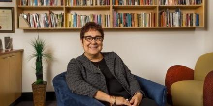 Distinguished Professor Aileen Moreton-Robinson sitting in front of a bookshelf