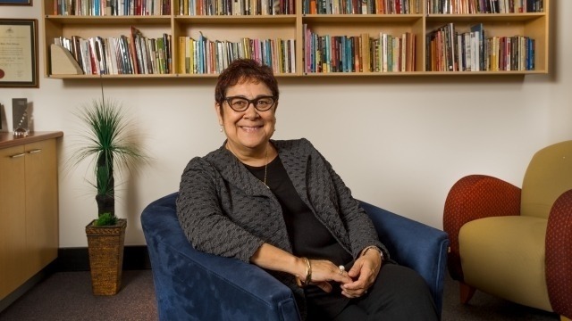 Distinguished Professor Aileen Moreton-Robinson sitting in front of a bookshelf