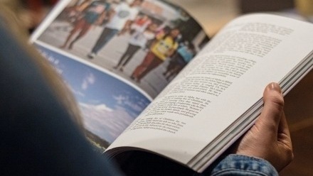 A person is holding a publication open with colour photos and writing